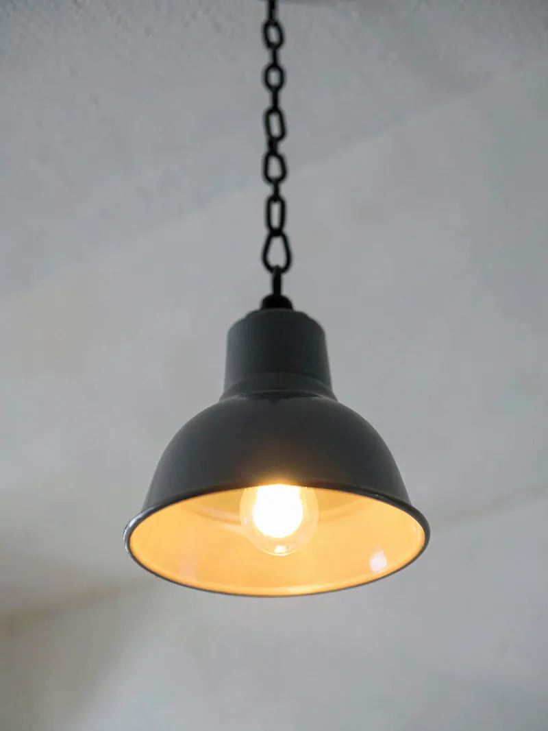 A dark grey enamel industrial pendant lamp hanging on a chain against a white ceiling